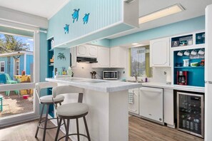 A modern kitchen with a central island, white cabinets, and a view of a blue house outside.