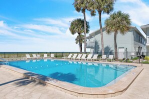 Ein Pool mit Liegestühlen und Palmen, umgeben von einem Gebäude mit Blick aufs Meer.
