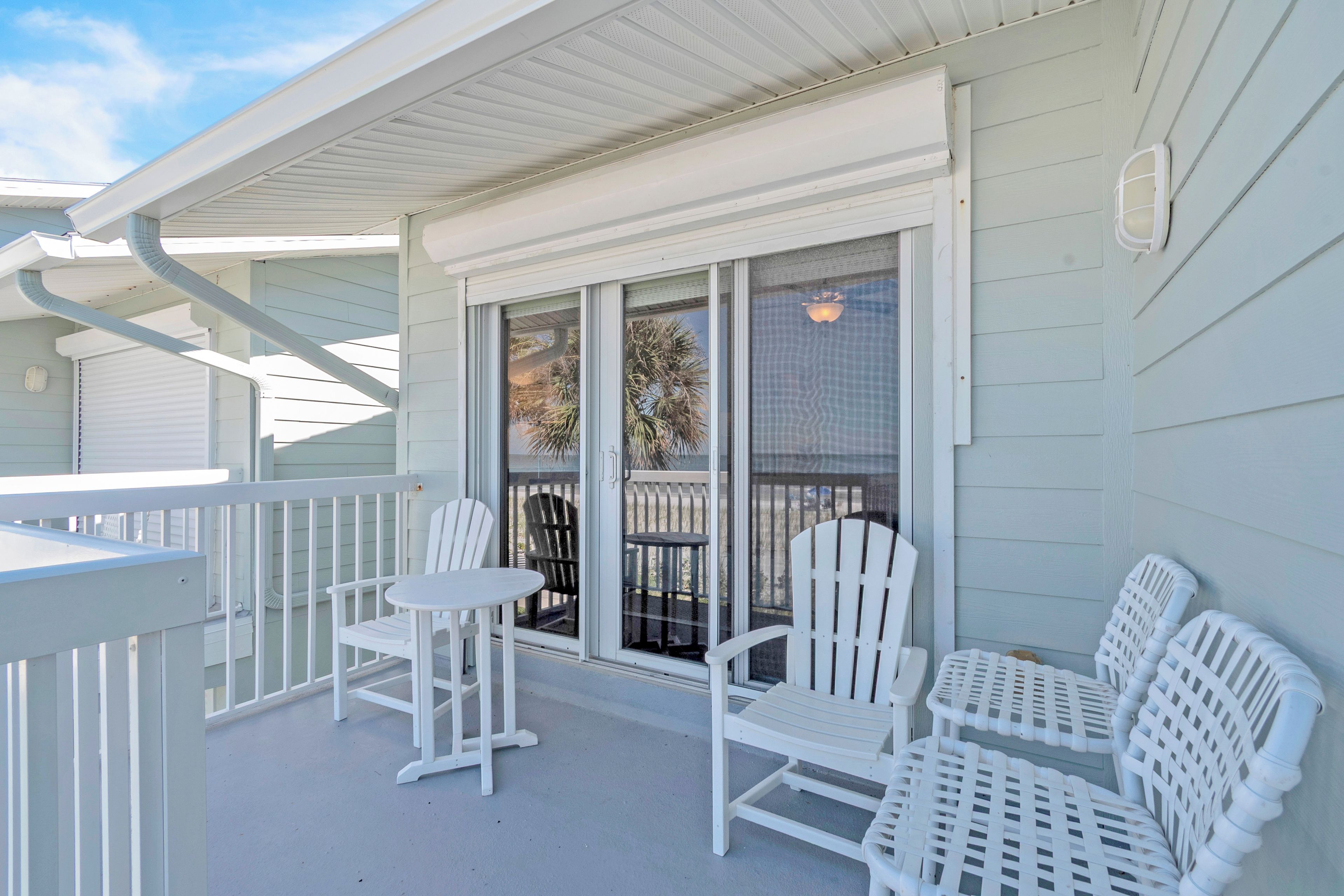 A covered outdoor area with white railings, a sliding glass door, and white outdoor furniture.