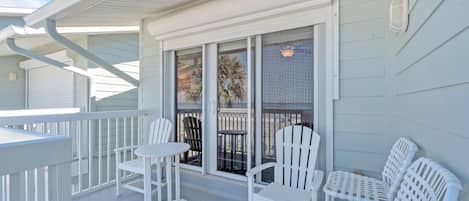 A covered outdoor area with white railings, a sliding glass door, and white outdoor furniture.