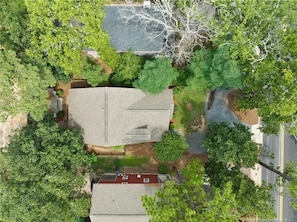 An aerial view of a residential area with a house featuring a sloped roof, surrounded by dense greenery and a road. - Charming Walkable Downtown Southern Pines 3 bed/2-1/2 Bath! (Southern Pines)