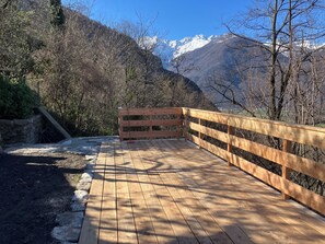 Eine Holzbrücke mit Geländer, die in eine gebirgige Landschaft mit schneebedeckten Gipfeln führt.