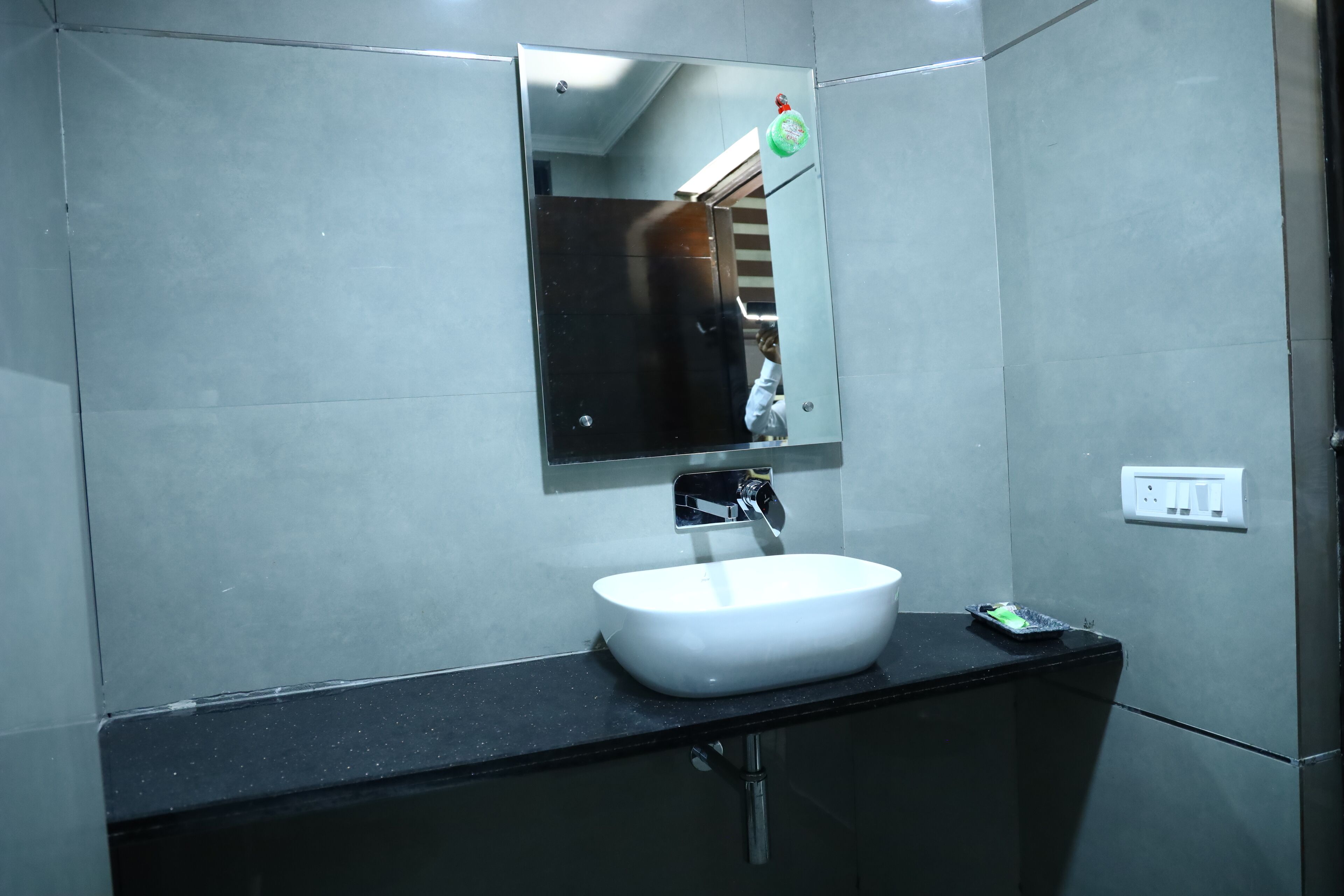Une salle de bain avec un lavabo blanc, un miroir et un plan de toilette noir.