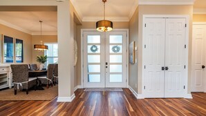 A hallway with a dining area, wooden flooring, and a double door with frosted glass panels. - Coral Oasis: Screened Lanai with Private Heated Pool & Spacious 4-Bed Retreat (Cape Coral)