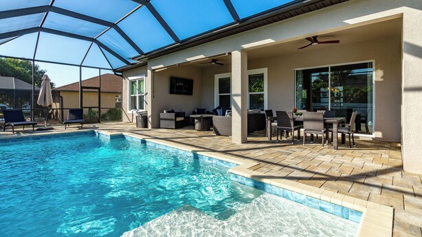 A swimming pool with a glass ceiling, outdoor seating, and a ceiling fan. - Coral Oasis: Screened Lanai with Private Heated Pool & Spacious 4-Bed Retreat (Cape Coral)