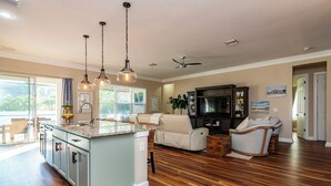 A spacious living area with a kitchen island, a seating area with a sofa and chairs, and a dining area with a table and chairs. - Coral Oasis: Screened Lanai with Private Heated Pool & Spacious 4-Bed Retreat (Cape Coral)