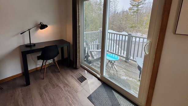 Et værelse med skrivebord, stol og en stor skydedør, der fører ud til en udendørs terrasse.