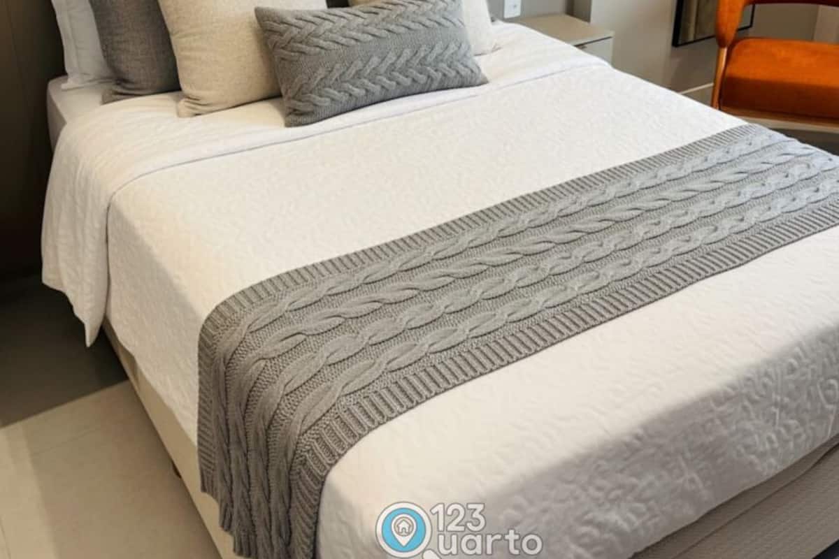 A neatly made bed with a white and gray blanket, a gray knitted throw, and several pillows in shades of white and gray.