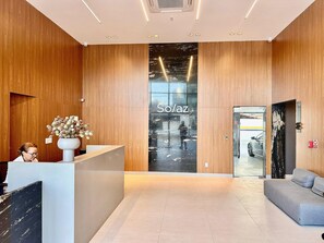 A modern reception area with a wooden finish, a reception desk, a large glass window, and a sofa. - Solaz Smart Living  (João Pessoa)