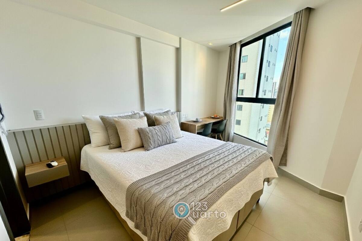 A modern hotel room with a large bed, bedside tables, a desk, and a window with a city view.