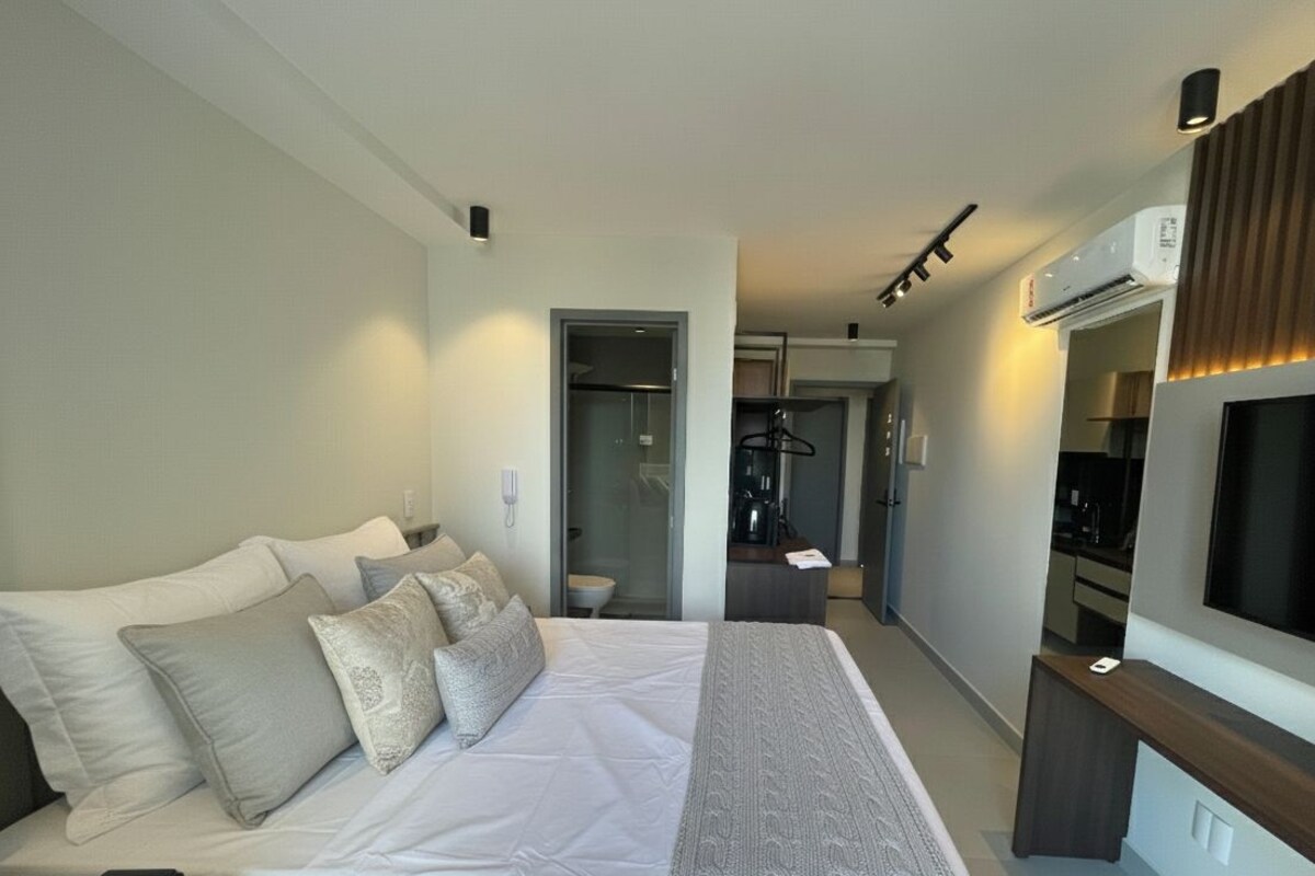 A hotel room with a bed, a TV, a desk, and a bathroom visible through an open door.