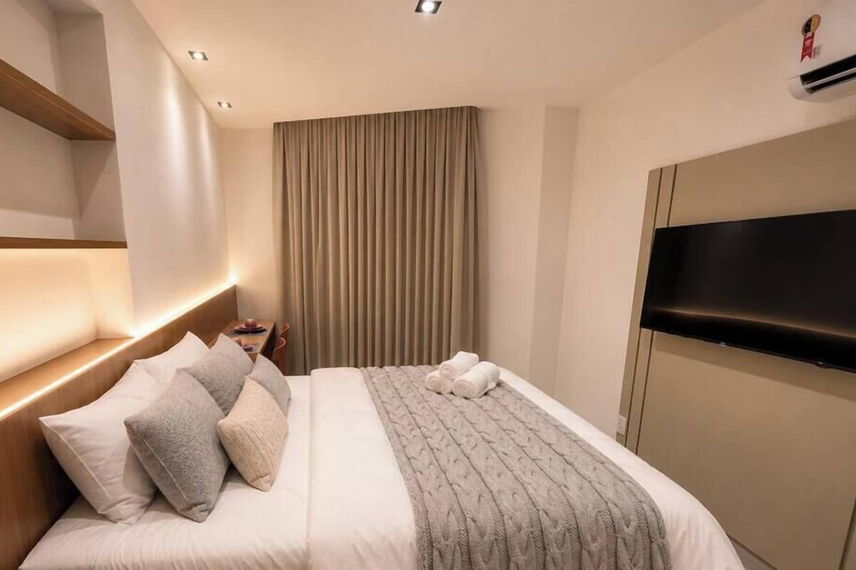 A hotel room with a bed, headboard, bedside table, curtains, and a TV.