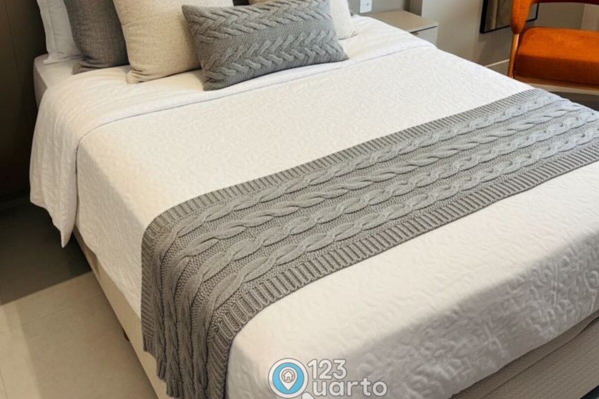 A neatly made bed with a white and gray blanket, a gray knitted throw, and several pillows in shades of white and gray.