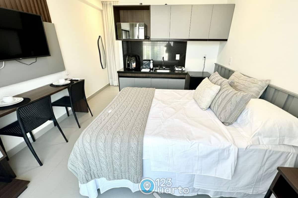 A hotel room with a bed, a desk, a TV, a kitchenette, and a bathroom.