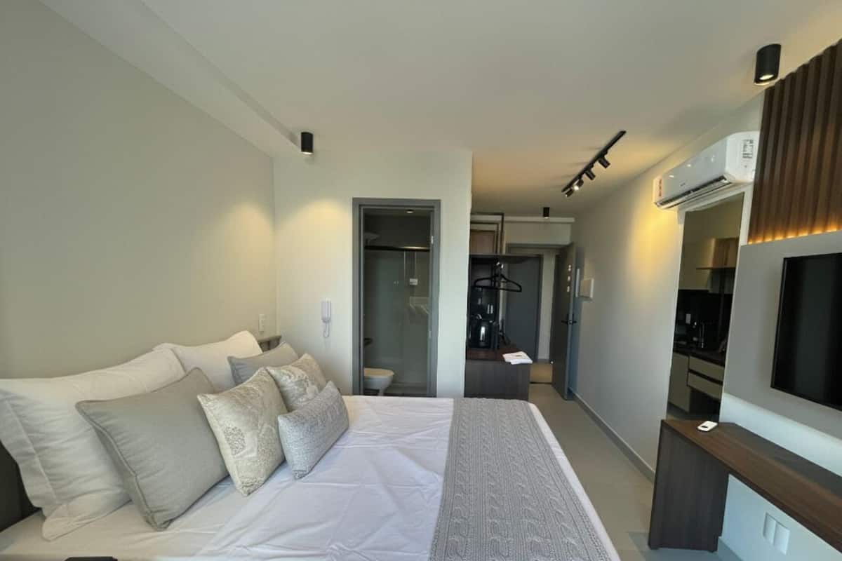 A hotel room with a bed, a TV, a desk, and a bathroom visible through an open door.