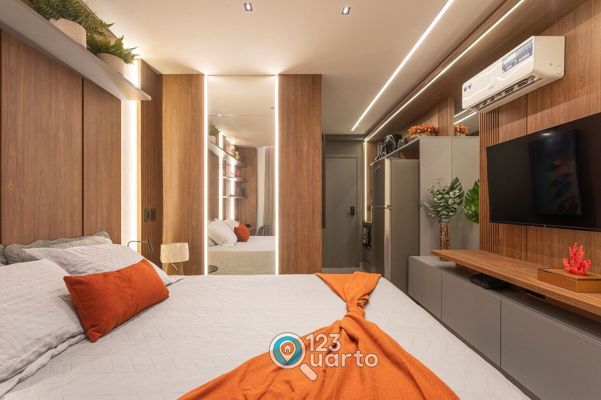 A modern hotel room with a bed, TV, and built-in air conditioning unit.