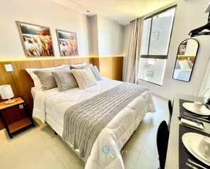 A hotel room with a bed, a bedside table with a lamp, a mirror, a window with curtains, and a view of the outside. - Solaz Smart Living  (João Pessoa)