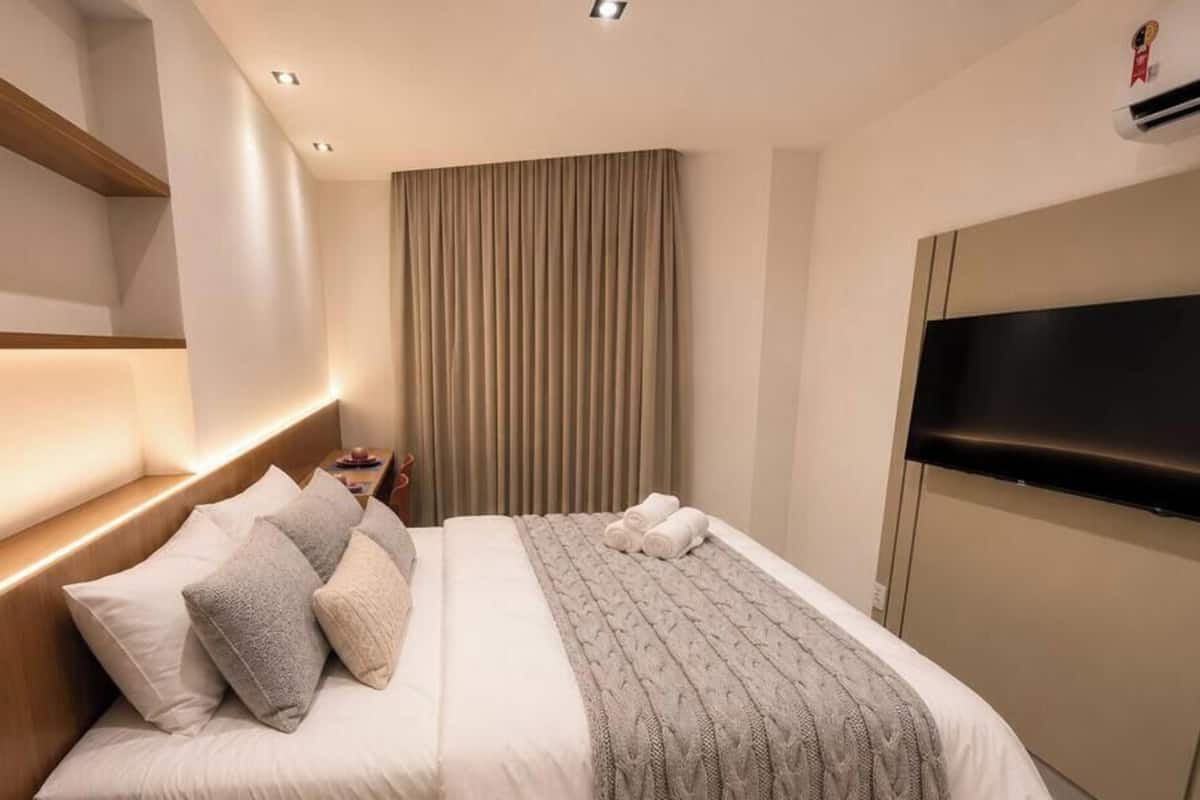A hotel room with a bed, pillows, a TV, and a curtain.