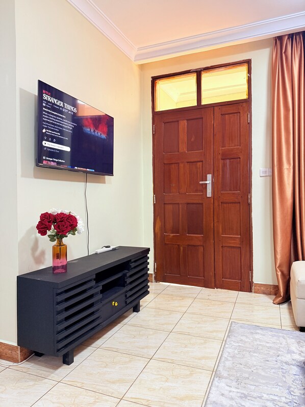 A living room with a flat-screen TV mounted on the wall, a wooden door, and a black entertainment unit.