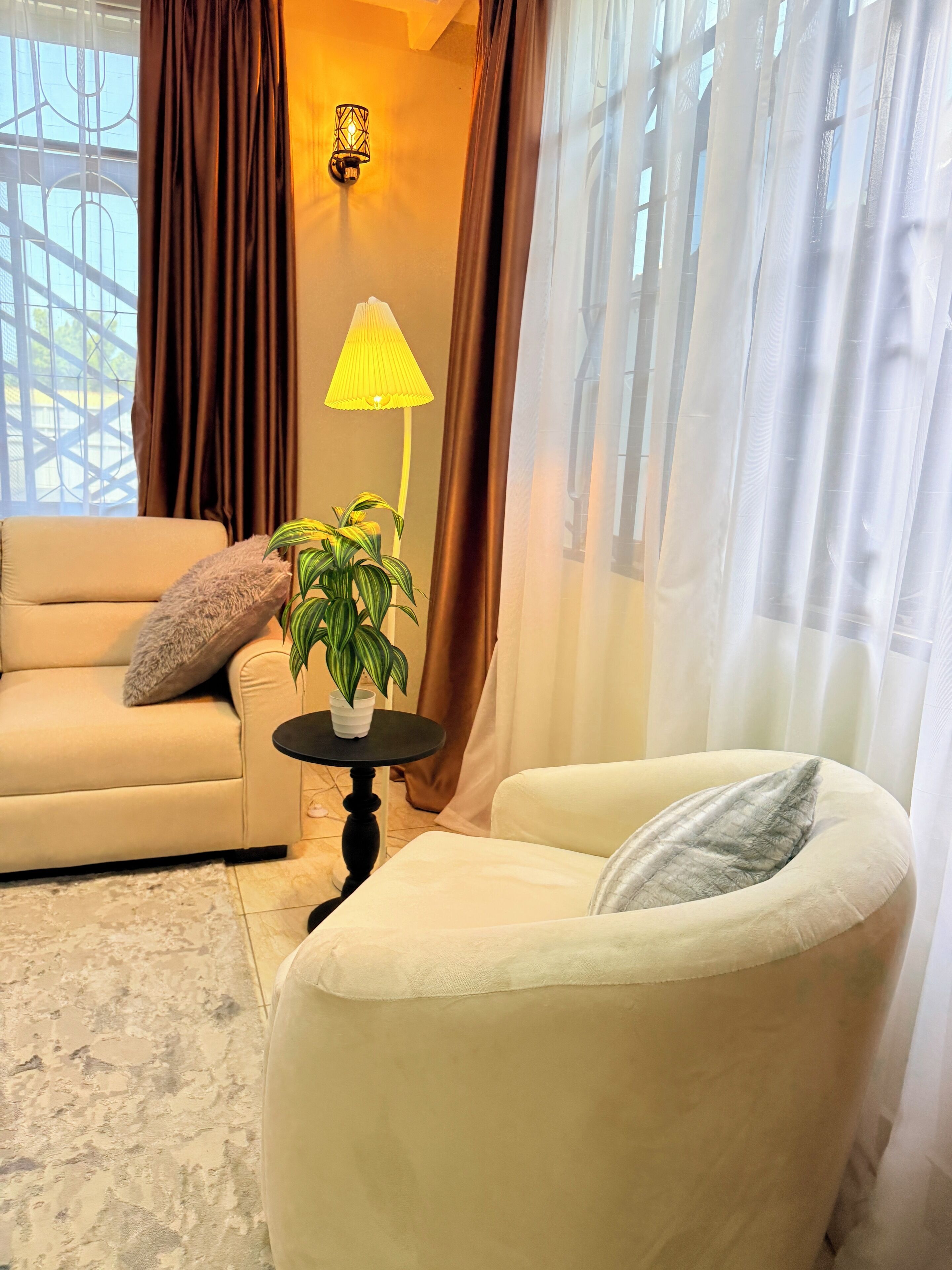 Una sala de estar con un sofá color beige, una mesa redonda con una planta y un sillón blanco.