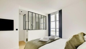 Een moderne slaapkamer met een bed, een grote spiegel en een raam met gordijnen.