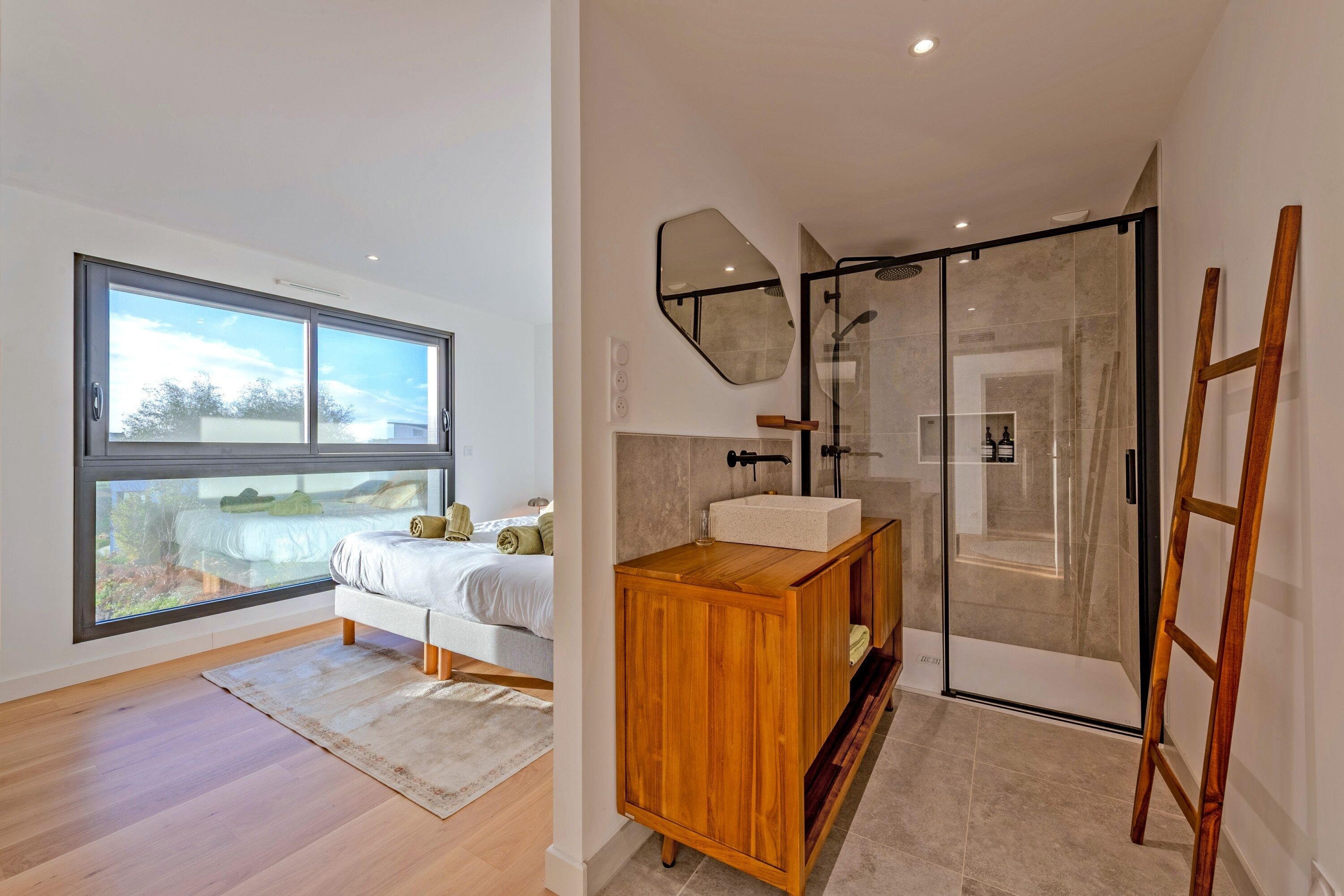 A modern bathroom with a glass shower, wooden vanity, and a large window.