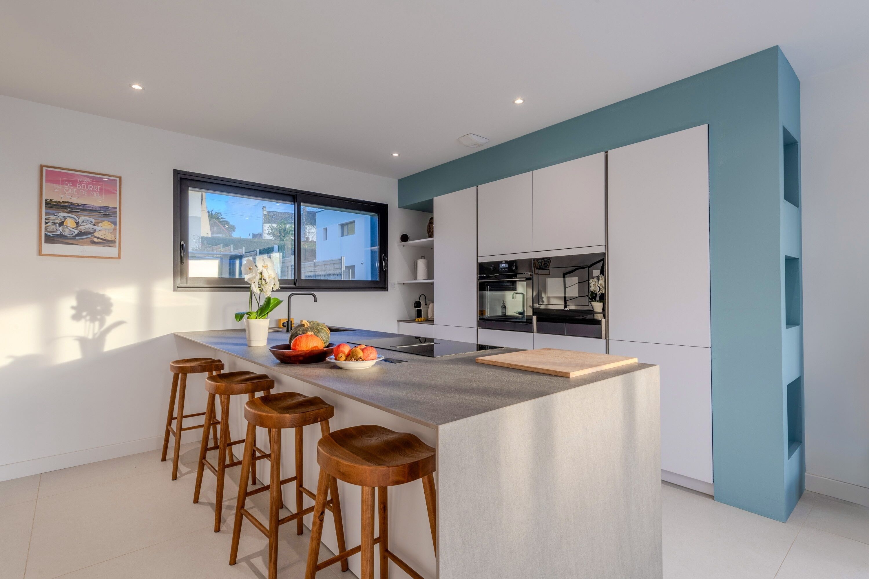 A modern kitchen with a central island, bar stools, and a window overlooking a building.