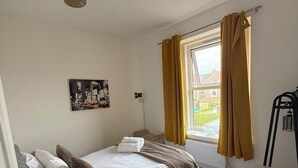 A bedroom with a bed, a window with curtains, a radiator, and a wall-mounted light fixture. - Newly Redecorated 1 bed flat ! (Weston-Super-Mare)
