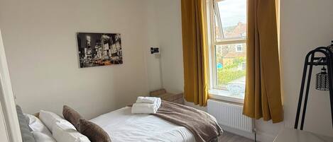 Une chambre à coucher avec un lit, une fenêtre avec des rideaux, un radiateur et un luminaire fixé au mur.