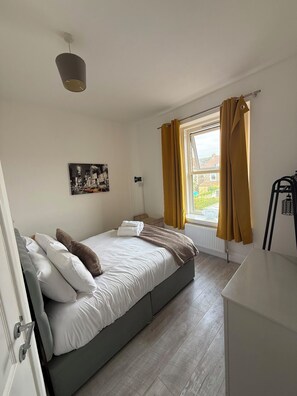 A bedroom with a bed, a window with curtains, a radiator, and a wall-mounted light fixture. - Newly Redecorated 1 bed flat ! (Weston-Super-Mare)