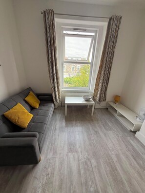 A modern living room with a sofa, a small table, and a view through a window. - Newly Redecorated 1 bed flat ! (Weston-Super-Mare)
