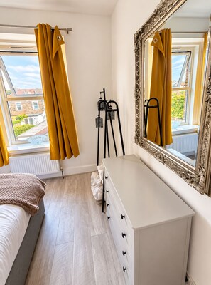 Une chambre à coucher avec un lit, une commode, un miroir et une fenêtre avec des rideaux.
