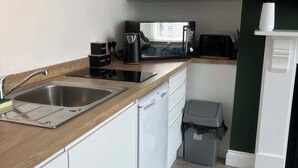 Een moderne keuken met een houten aanrecht, een RVS spoelbak, witte kastjes, een magnetron en een prullenbak.