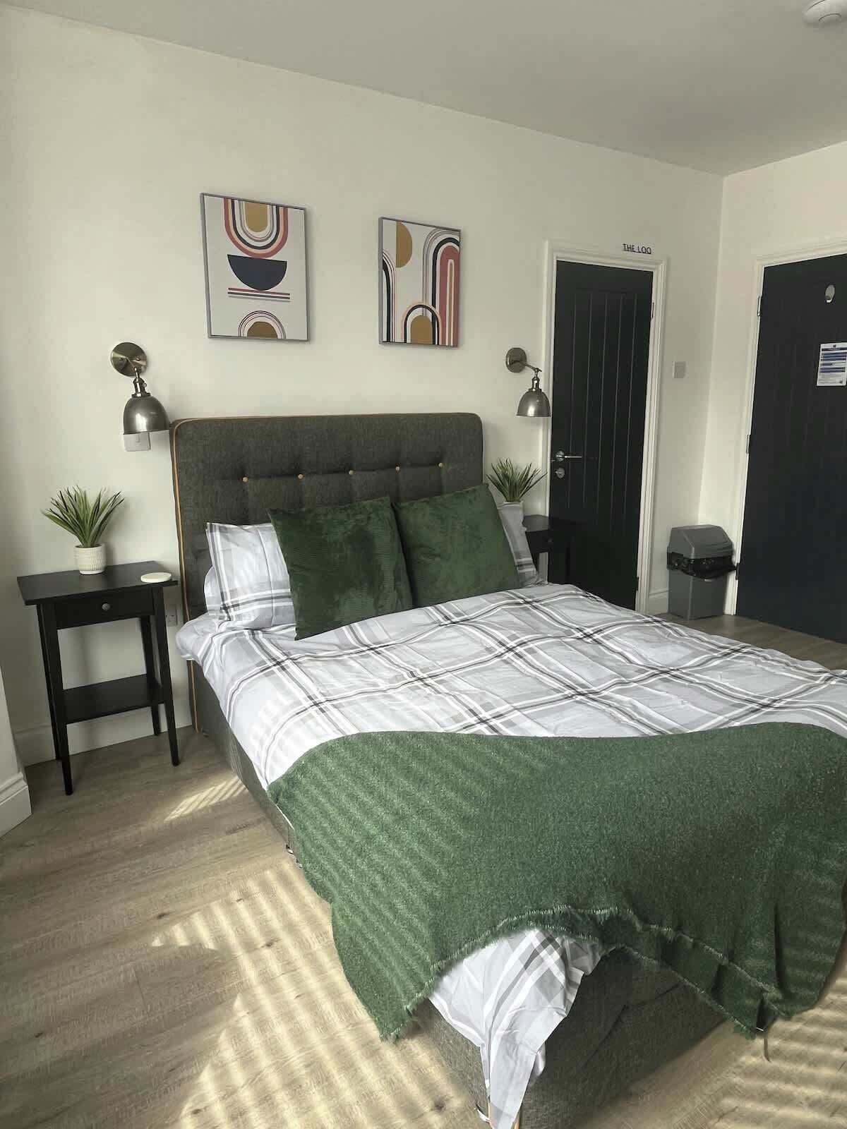 A bedroom with a bed, two bedside tables, two wall-mounted lamps, and two potted plants.