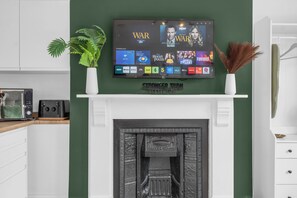 A modern living room with a flat-screen TV mounted above a fireplace, a potted plant, and decorative items. - 1st Floor 1 Bed Studio (Weston-Super-Mare)
