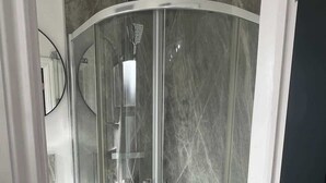 Een moderne douchecabine met een glazen deur, douchekop en een marmeren wand.