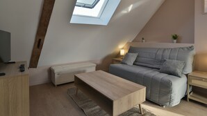 A modern loft bedroom with a sloped ceiling, a skylight, a grey sofa, a wooden coffee table, and a bedside table with a lamp. - Les Trois Rois 5 - Centre Avranches (Avranches)