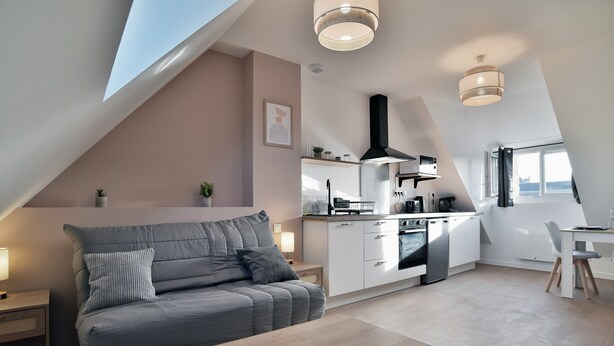 A modern loft apartment with a dining area, kitchenette, and a large window providing natural light. - Les Trois Rois 5 - Centre Avranches (Avranches)