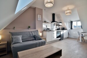 Moderni loft-tyylinen huoneisto, jossa on ruokailutila, pieni keittiö ja suuri ikkuna, josta tulee runsaasti luonnonvaloa.