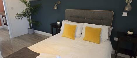 A neatly made bed with white and yellow pillows, a dark headboard, and a small bedside table with a lamp.