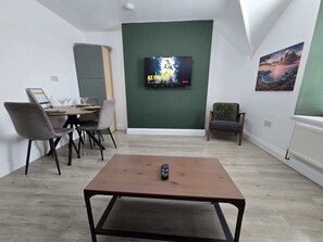 Ein Wohnzimmer mit Fernseher, Esstisch, Stühlen und einem Bild an der Wand.
