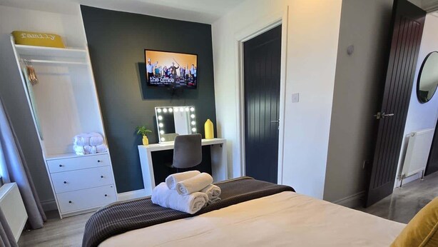 Una habitació d'hotel moderna amb un llit gran, una tocador amb mirall, una televisió i un armari.
