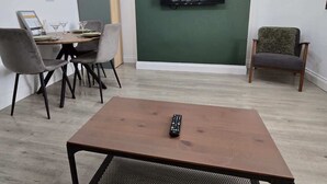 Un saló amb televisió penjada a una paret verda, una taula de centre i una zona de menjador amb cadires.