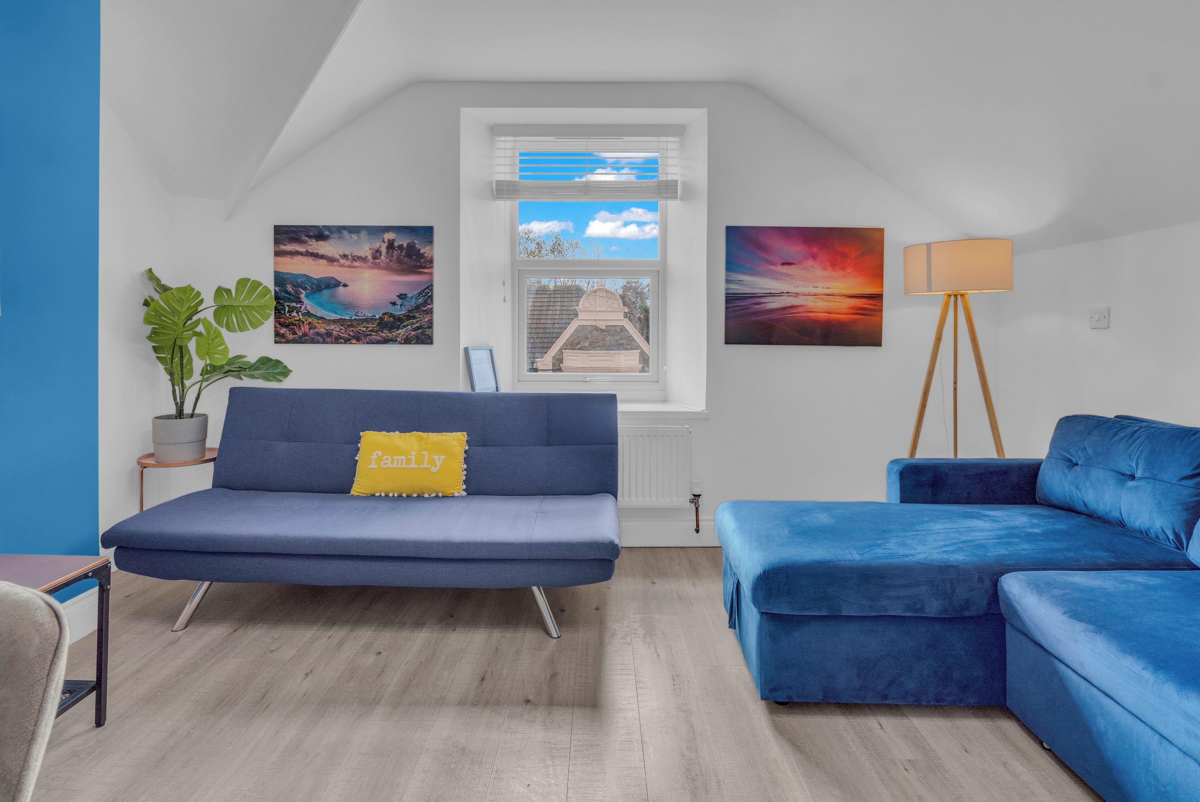 Un salon moderne avec un canapé bleu, un fauteuil bleu, une lampe sur pied et des œuvres d’art accrochées aux murs.