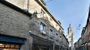 A narrow street with stone buildings, a visible shop with a sign 'Sol & Mani', and a church tower in the distance.