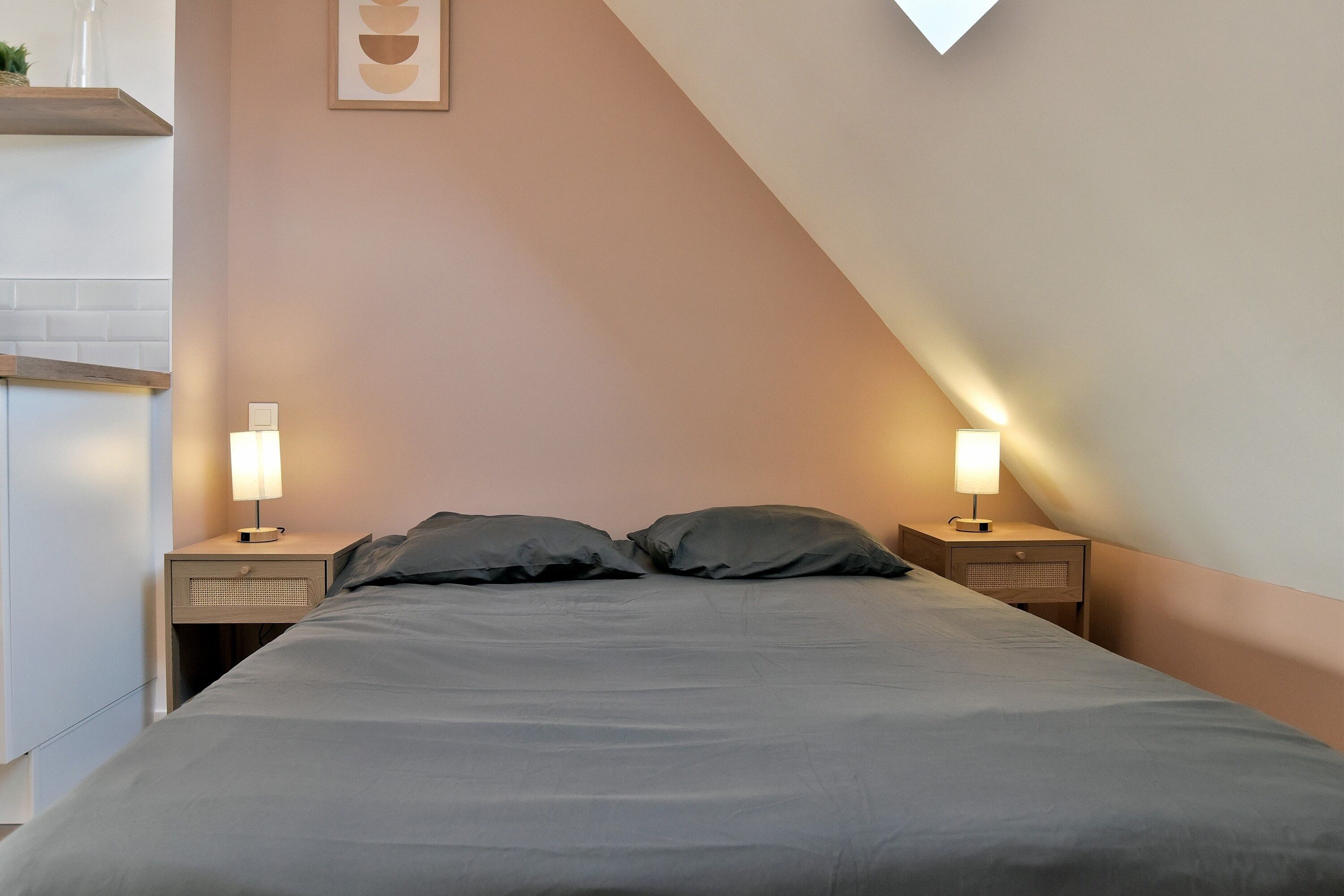 Une chambre à coucher comprenant un lit, deux tables de chevet avec des lampes, une étagère fixée au mur et un luminaire au plafond.