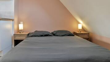 Une chambre à coucher comprenant un lit, deux tables de chevet avec des lampes, une étagère fixée au mur et un luminaire au plafond.
