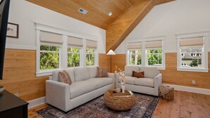 A spacious living room with two sofas, a round coffee table, and a large window with a view of greenery. - Award-Winner “The Carriage House”Gym+Pool Access (Powells Point)
