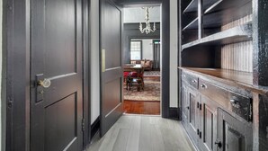 A hallway with a dark wooden door, a chandelier, and a dining area with a red rug. - Emma’s Cottage on Madison Avenue (Montgomery)