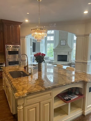 A spacious kitchen with granite countertops, stainless steel appliances, and a decorative chandelier. - Private Buckhead Estate Pool, Game Room, Custom Kitchen (Atlanta)